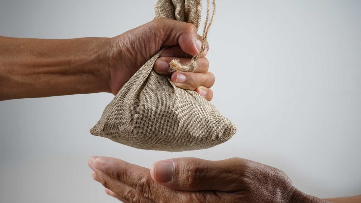 Hand holding small sack of coins giving to another hand