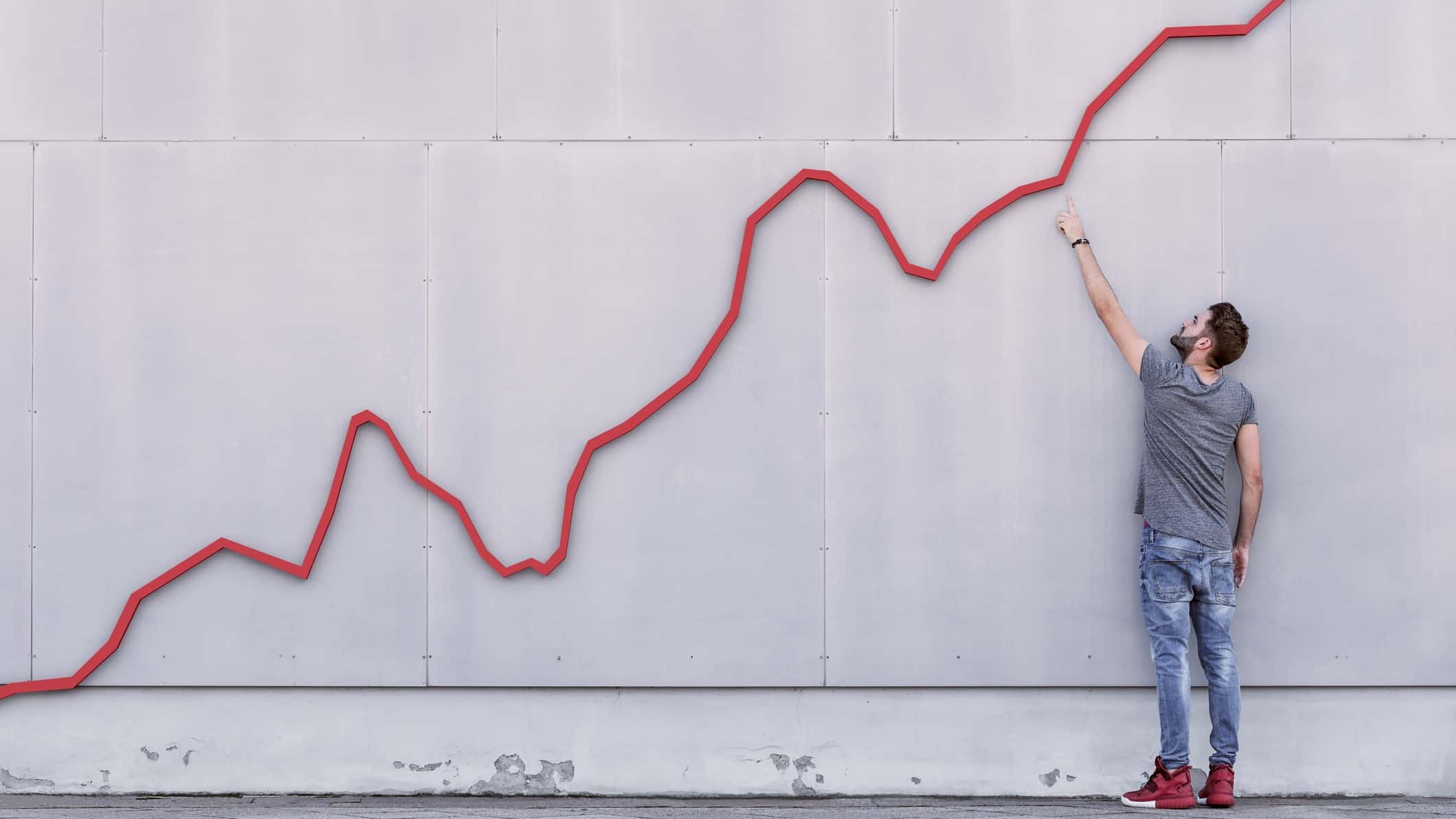 man pointing up at a rising red line which represents a growing share price