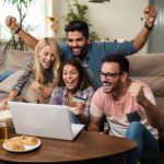 A group of happy young people watching sport on a laptop celebrate, indicating a win for sports betting bluebet