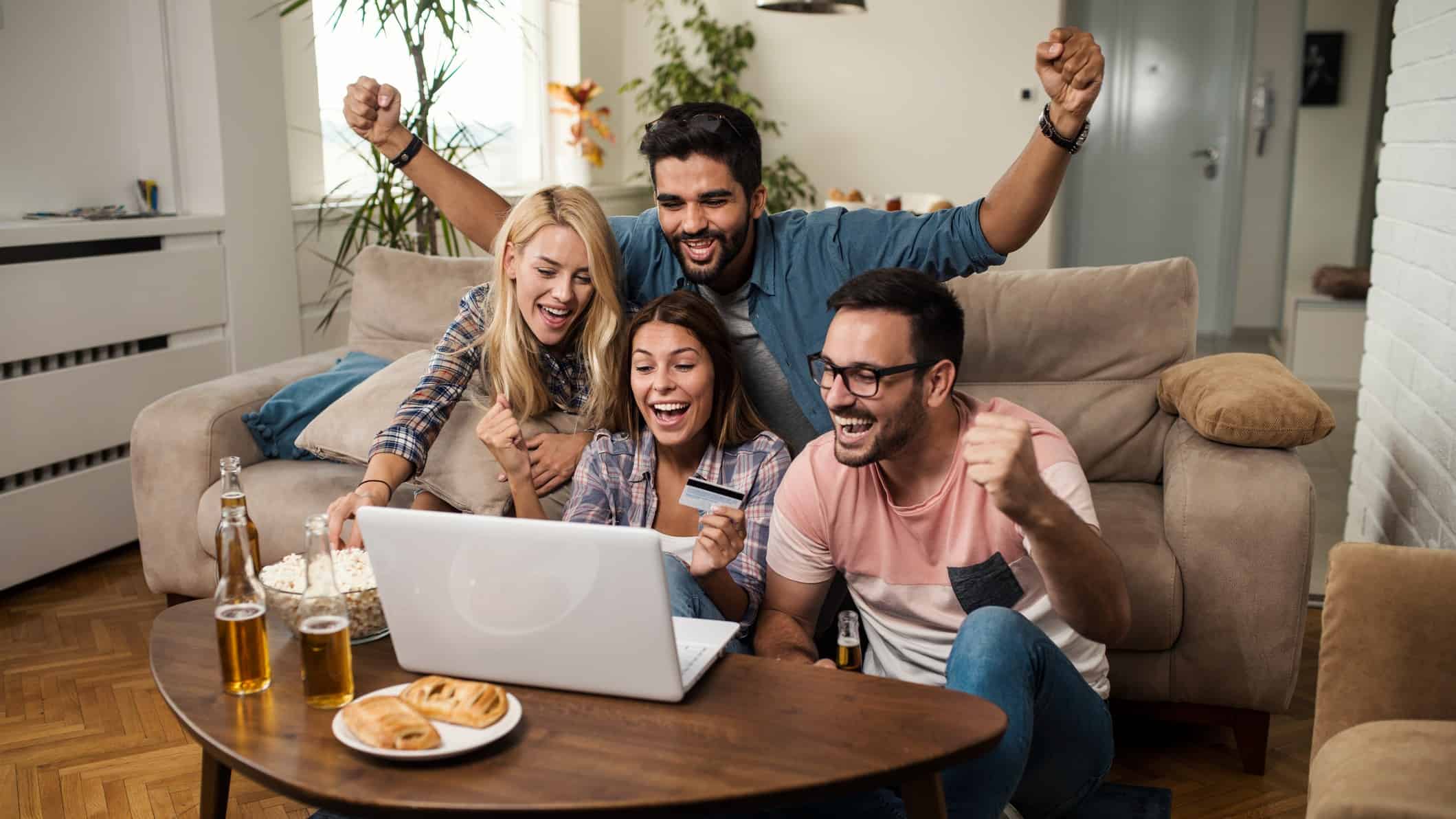 A group of happy young people watching sport on a laptop celebrate, indicating a win for sports betting bluebet