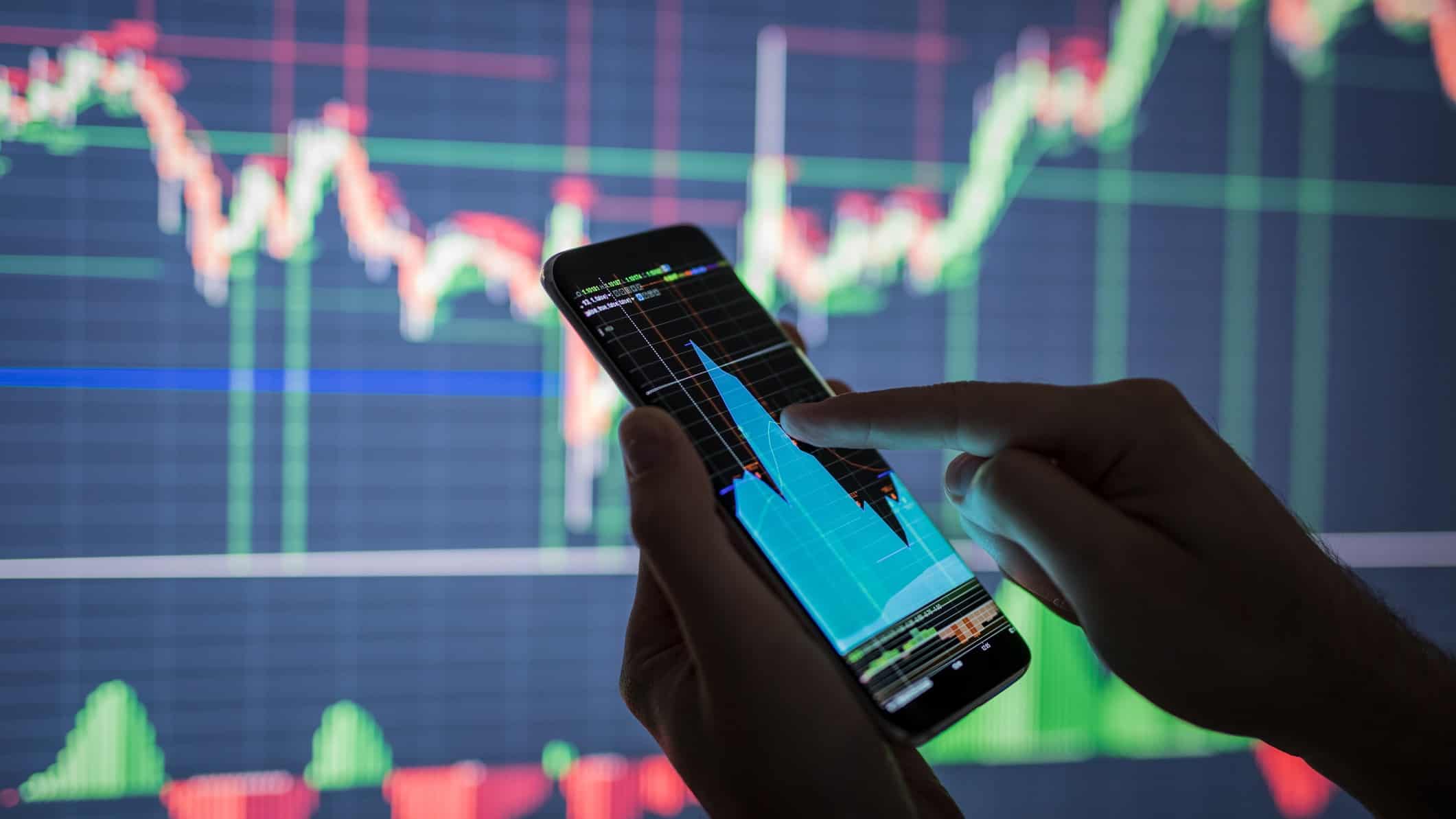 stockmarket graphic in background with man looking at stockmarket on phone