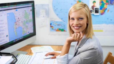 A smiling travel agent sitting at her desk working for Corporate Travel Management