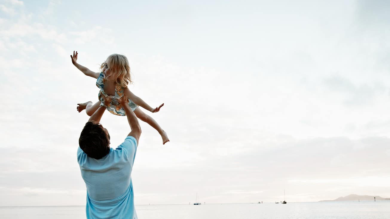 A dad flies his child up in the air with clouds in the backdrop