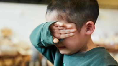 Little boy crying with his hand over his eyes.