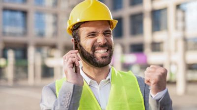 Ecstatic worker in suit and hard hat talking on phone