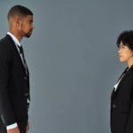 Two people in business attire, a man and a woman, stand facing each other solemnly.