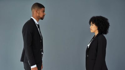 Two people in business attire, a man and a woman, stand facing each other solemnly.