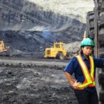 Female miner standing next to a haul truck in a large mining operation.