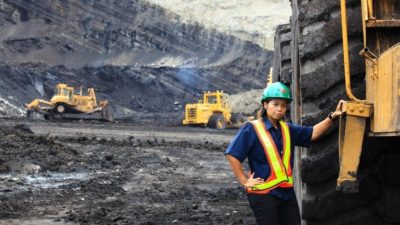 Female miner standing next to a haul truck in a large mining operation.