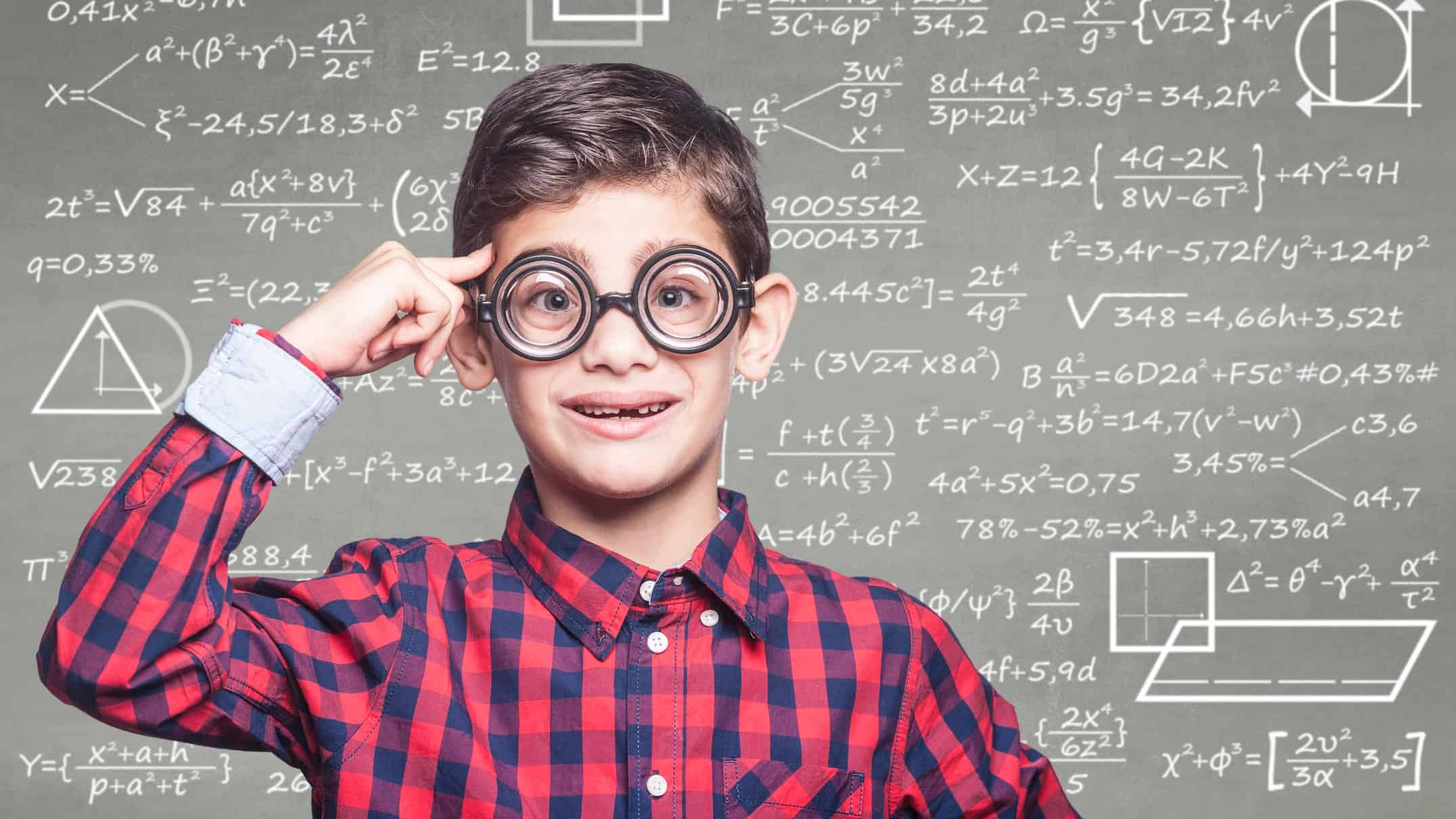School boy wearing glasses standing in front of chalk board with maths and share price calculations on it