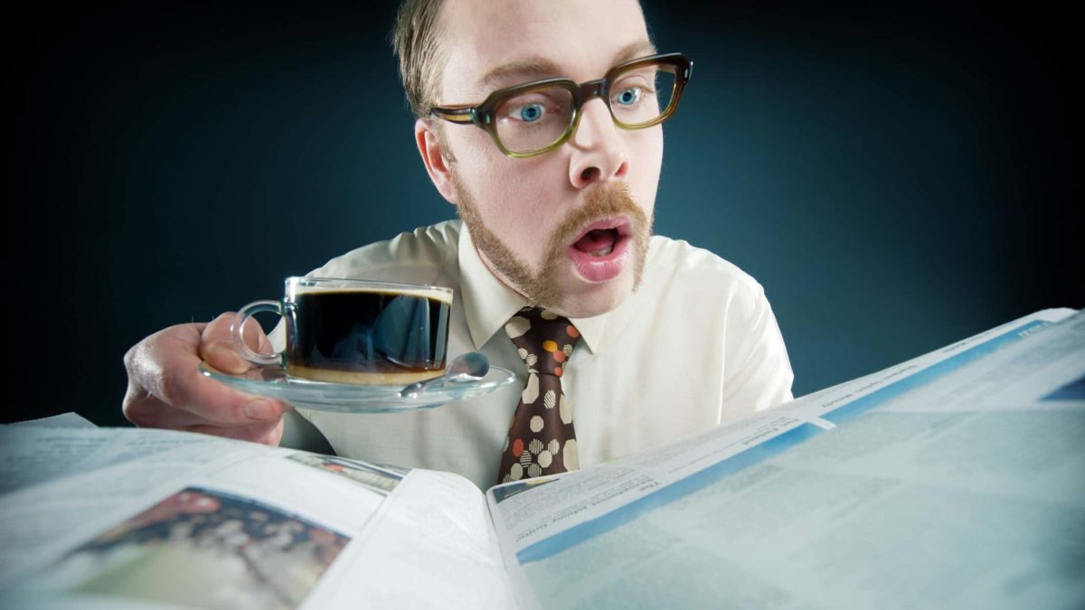A surprised and curious male investor drinks black coffee while reading the latest news on rising ASX shares in the newspaper