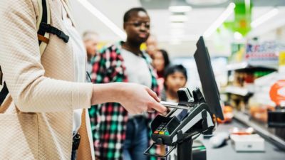 A woman uses her phone to pay at the counter, with a queue of more customers behind.