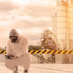 A uranium plant worker in full protective clothing squats near a radioactive warning sign at the site of a uranium processing plant.