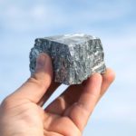 A hand holding a lump of rare earths material against a blue sky.