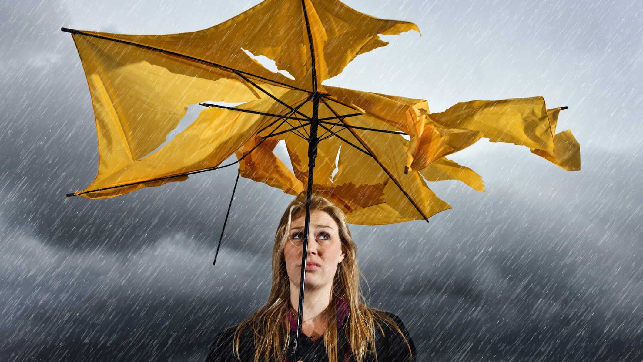 A woman with a sad face stands under a shredded umbrella in a grey thunderstorm