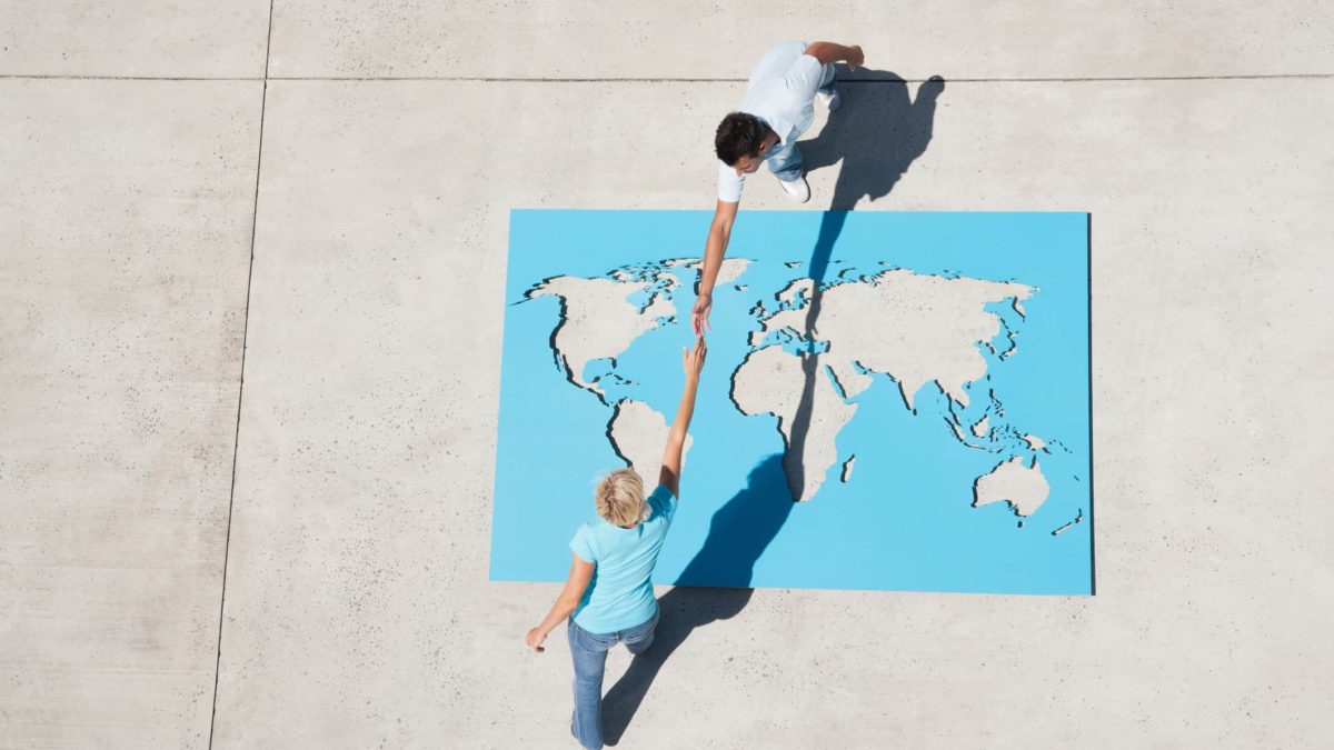 A map of the world on the pavement with two people shaking hands over it.