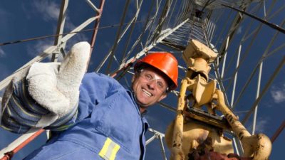 happy miner, happy oil and gas worker with thumb raised wearing a hard hat amid rigging