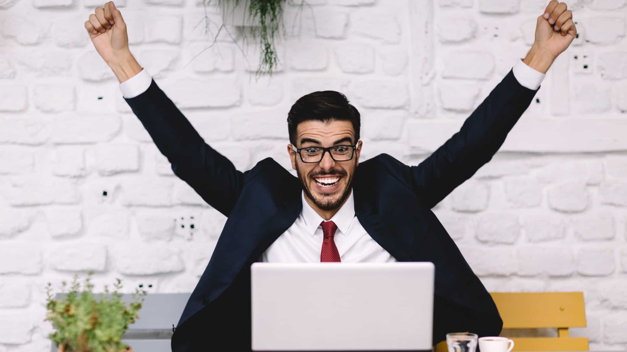 Businessman cheering at desk with arms in the air