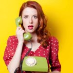 A young woman in a red polka-dot dress holds an old-fashioned green telephone set in one hand and raises the phone to her ear representing the Telstra share price and the opportunity for investors in FY23
