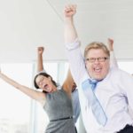 Happy business people raise their hands in celebration in an office environment.