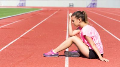 sad, unhappy athlete sitting on athletic track with head in hands, sports company share price fall