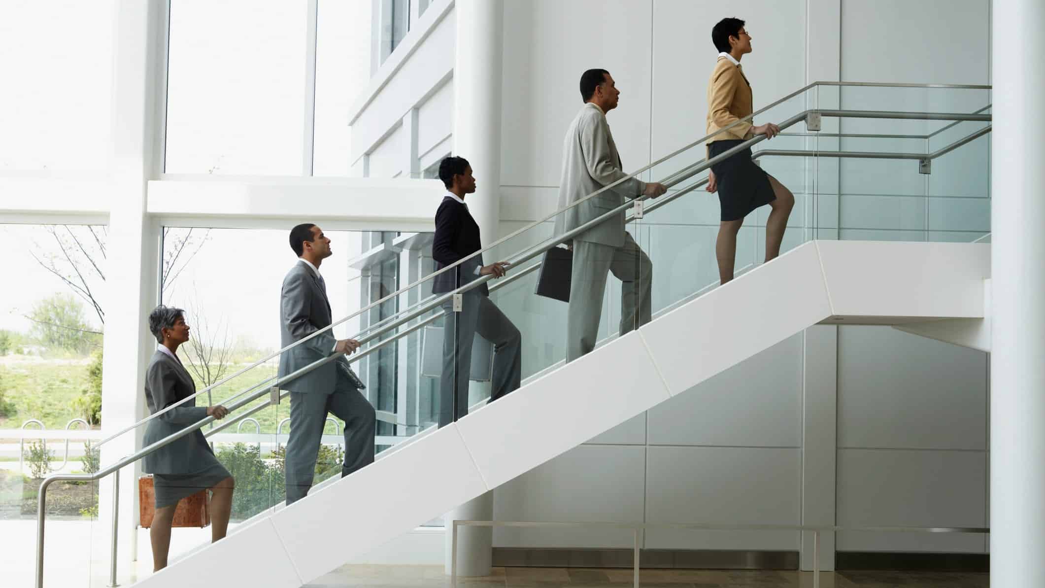 Five businessmen in suits walking up stairs in neat succession