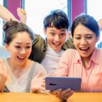 A group of friends cheer around a smart phone.