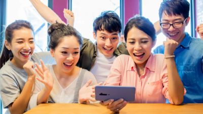 A group of friends cheer around a smart phone.