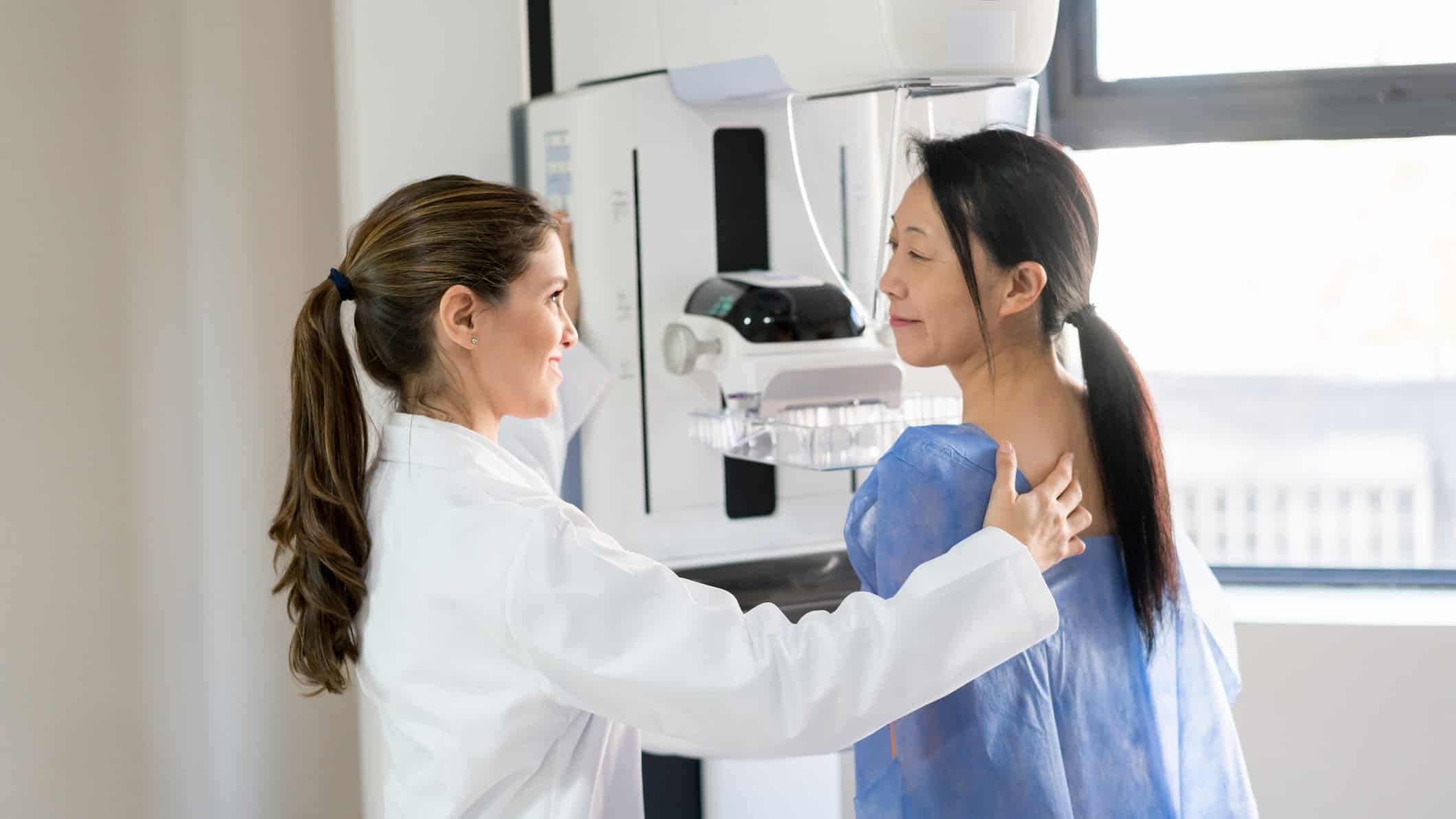 Woman preparing to have her breast screened with the support of a young female doctor.