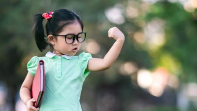 Young girl wearing glasses flexes her left bicep confidently.