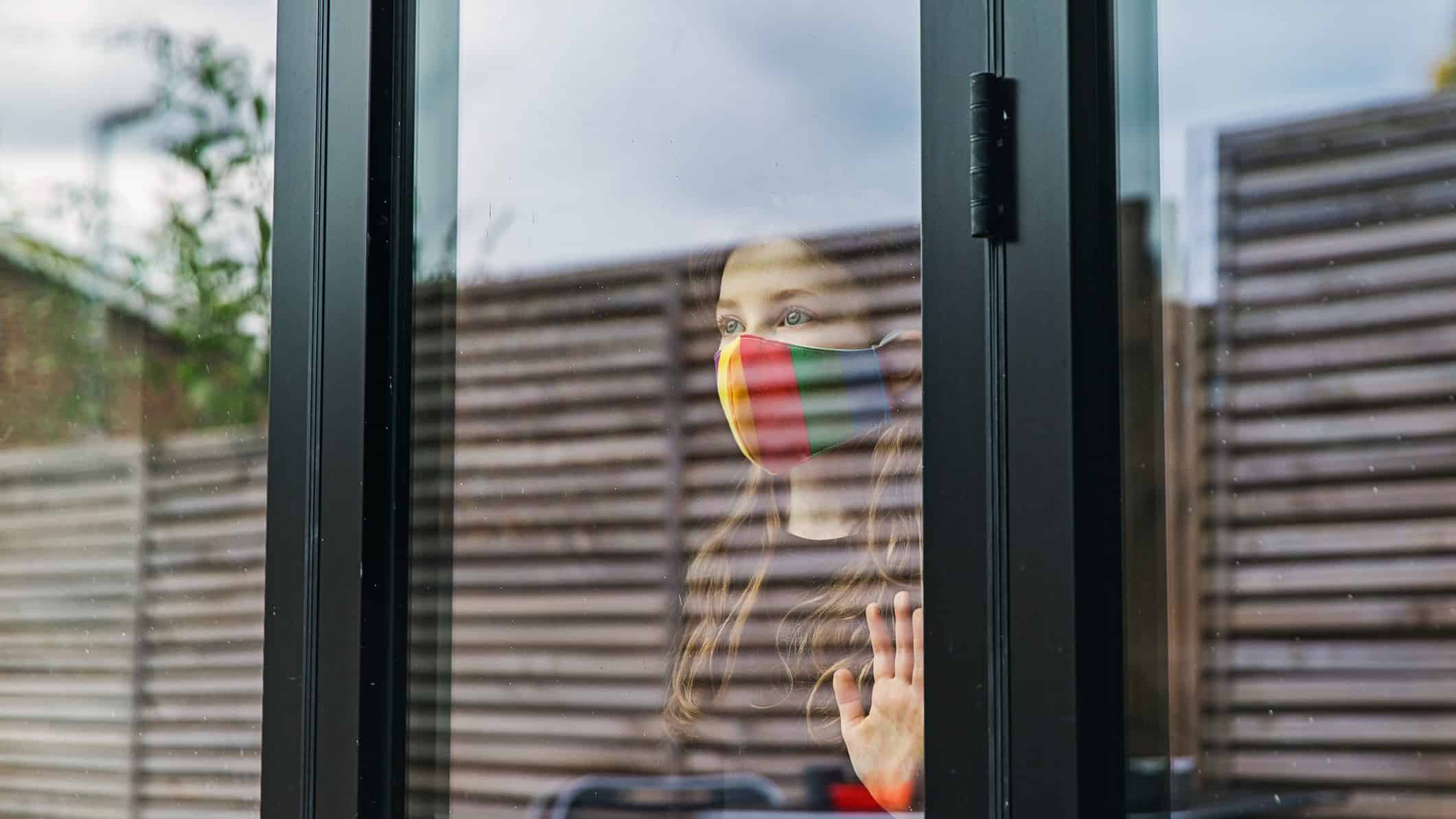 person wearing face mask looking out a window from indoors