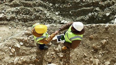 Looking down on two African workers shaking hands over an agreement in an open pit mine.