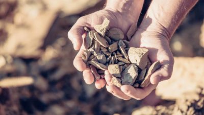 Two hands hold rocks while more rocks and earth appear in the background.