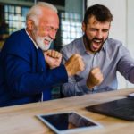 Two men looking at laptop and cheering.