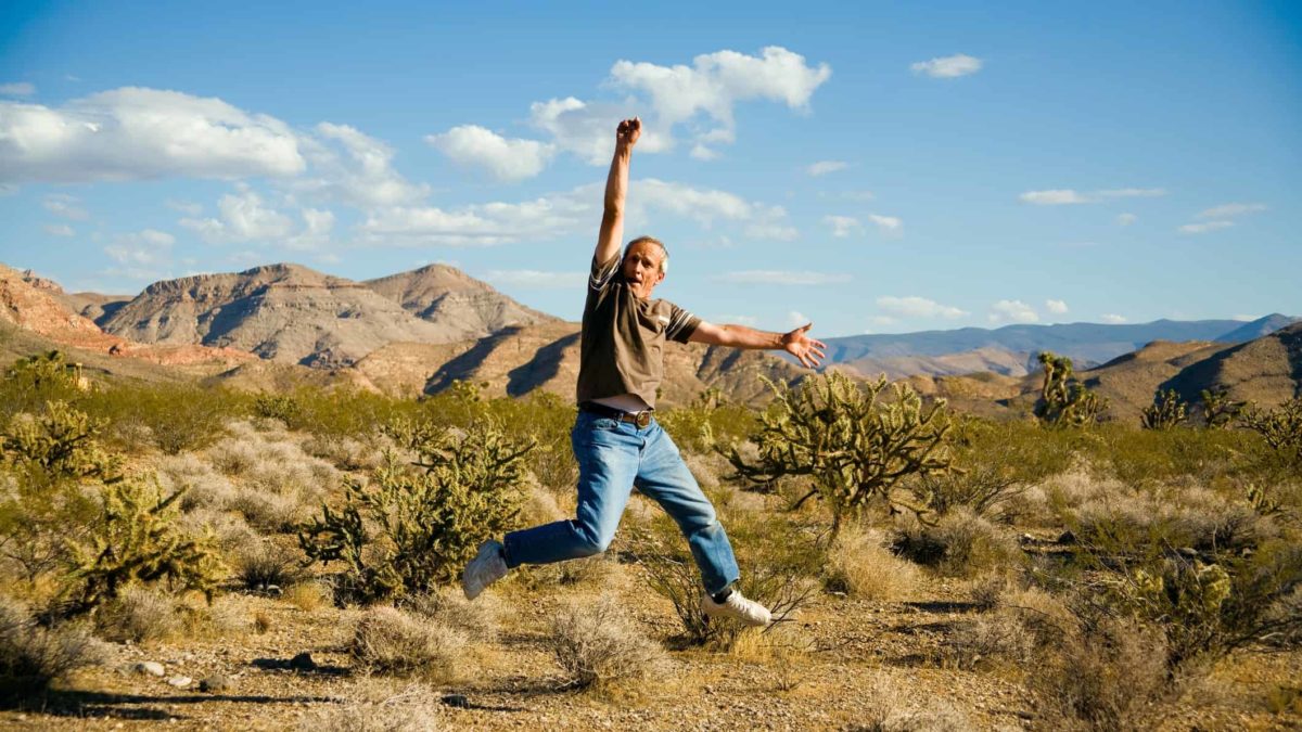An older man leaping into the air with joy in the Australian outback.