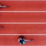 Birdseye view of four women racing in wheelchairs on an athletic track.