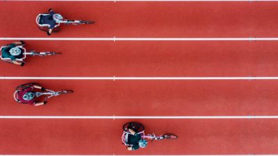Birdseye view of four women racing in wheelchairs on an athletic track.