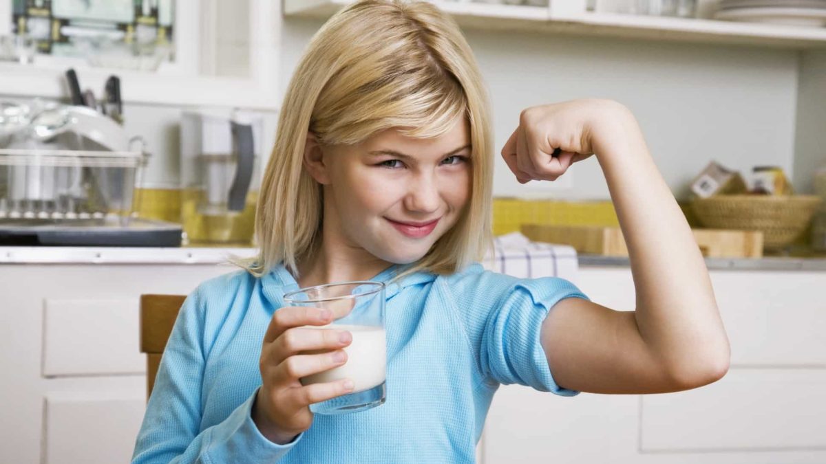 Young girl drinking milk showing off muscles.
