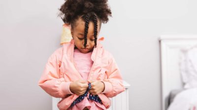 Little girl looking down trying to zip up her pink windcheater.