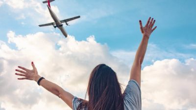 A woman holds her arms out as a plane flies overhead