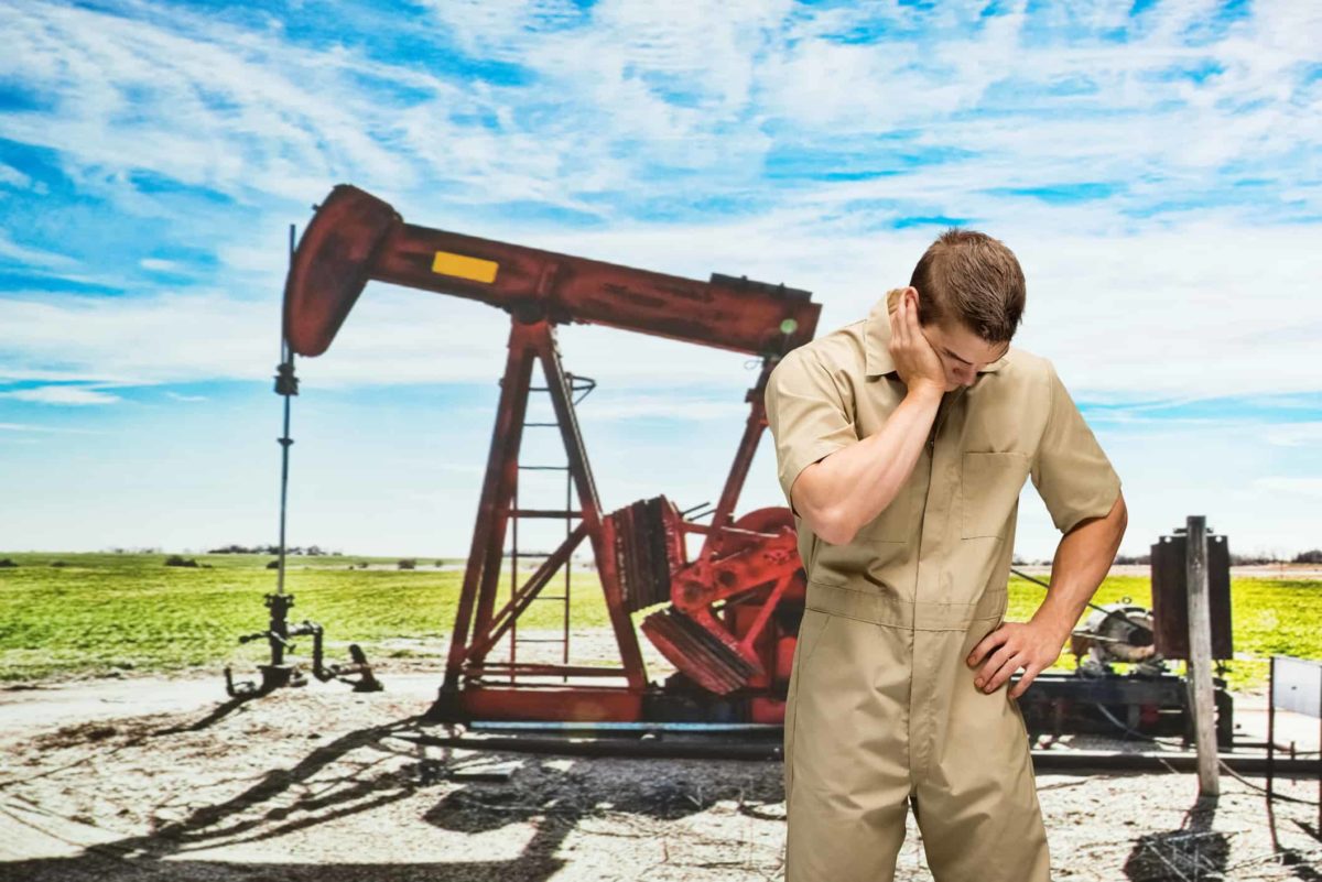 sad looking petroleum worker standing next to oil drill