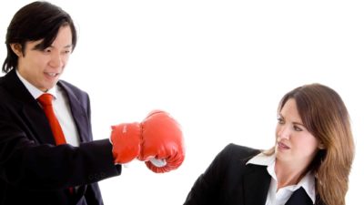 businessman wearing a boxing glove attempting to punch a business woman as she dodges