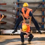 A happy construction worker leap-frogs over another as a third looks on