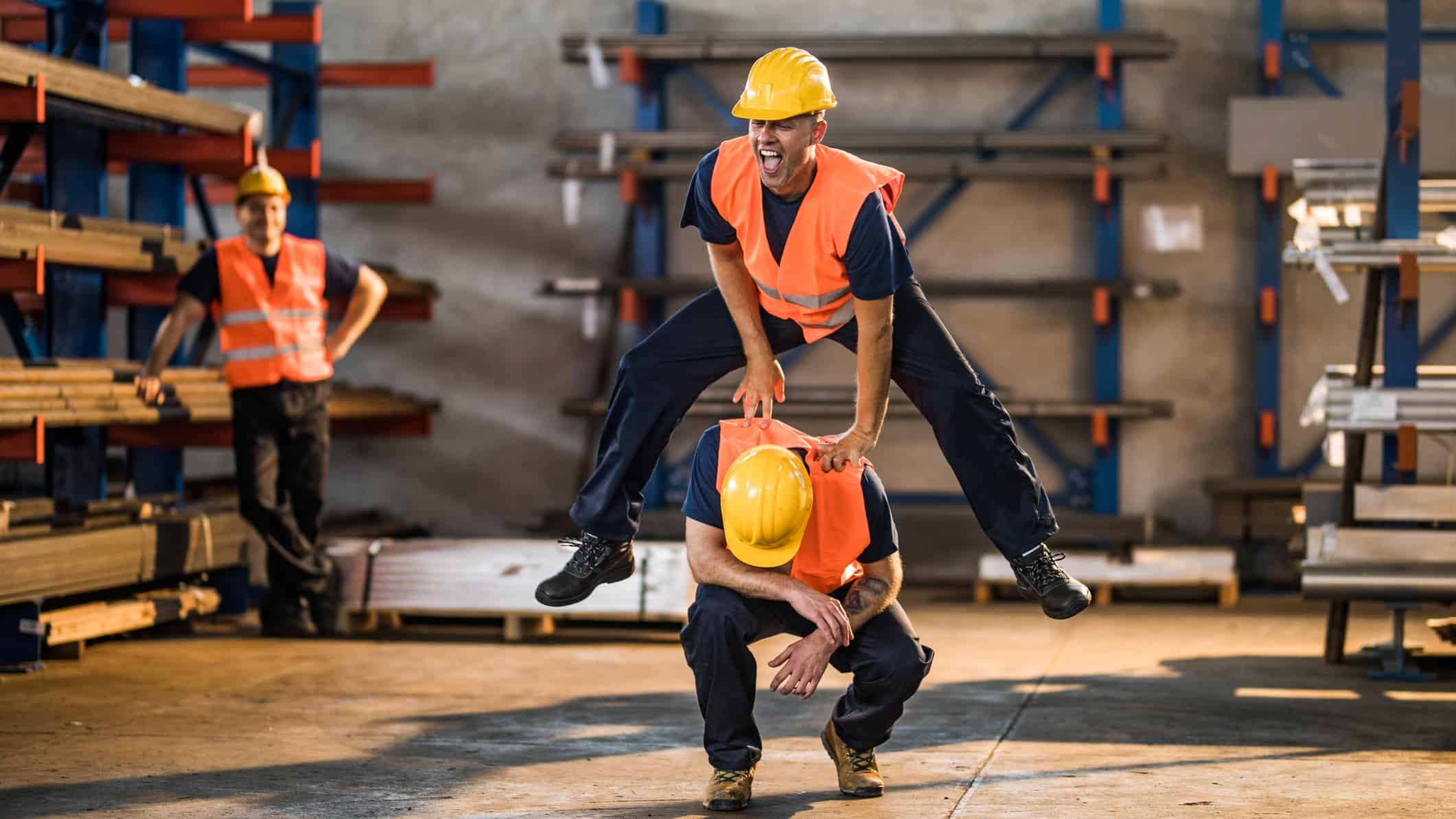 A happy construction worker leap-frogs over another as a third looks on