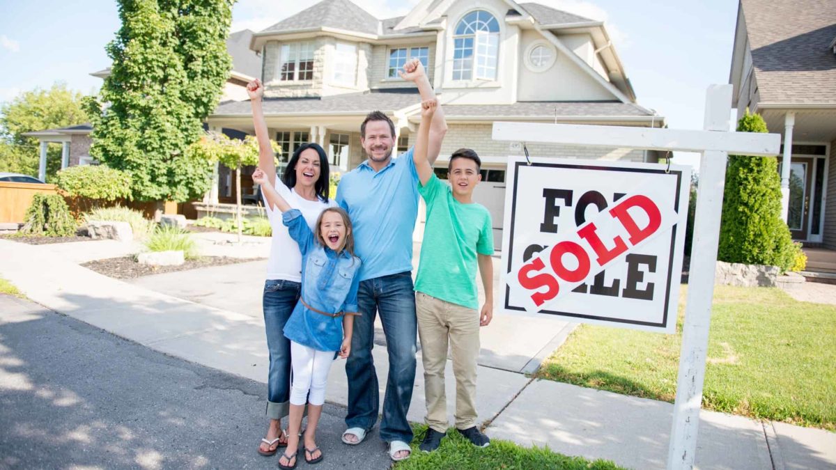 Happy family stands in front of new home in front of sold sign