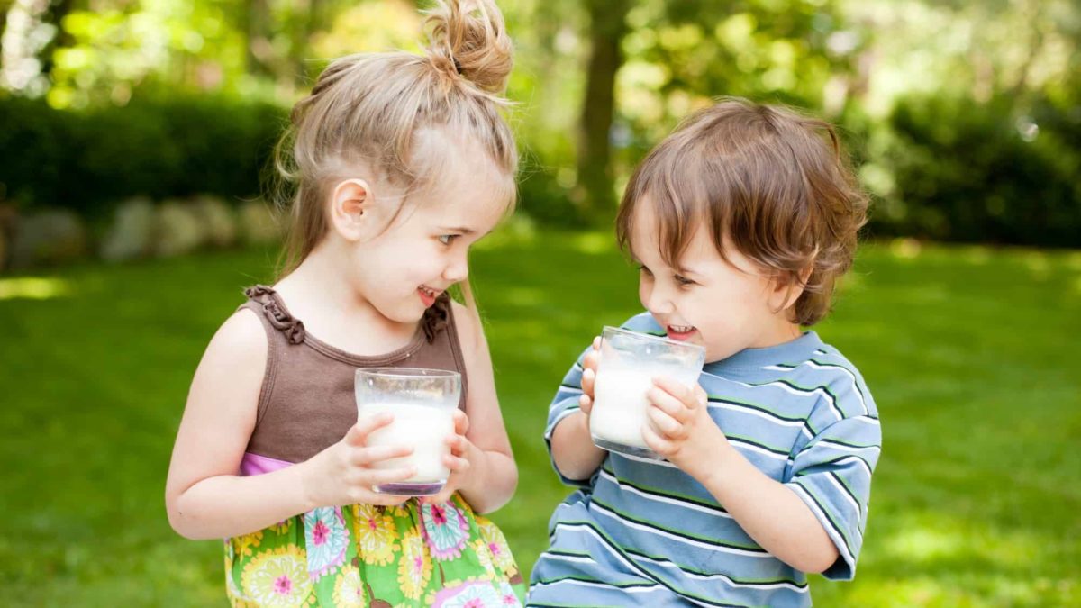A young girl and boy drinking milk in a garden setting