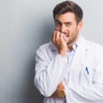 A healthcare worker wearing a white coat holds his fingers to his mouth looking worried as healthcare stocks like Cochlear crash today