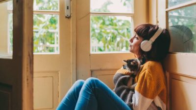 A woman in lockdown cuddles her cat and listens to music on her headphones