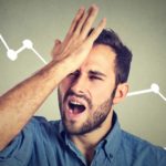 A man stands in front of a chart with an arrow going down and slaps his forehead in frustration.