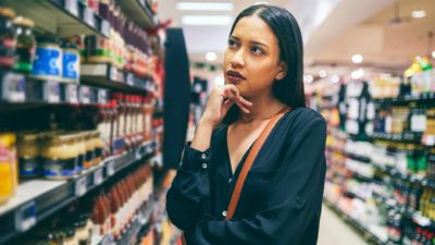 A woman ponders over what to buy as she looks at the shelves of a supermarket.